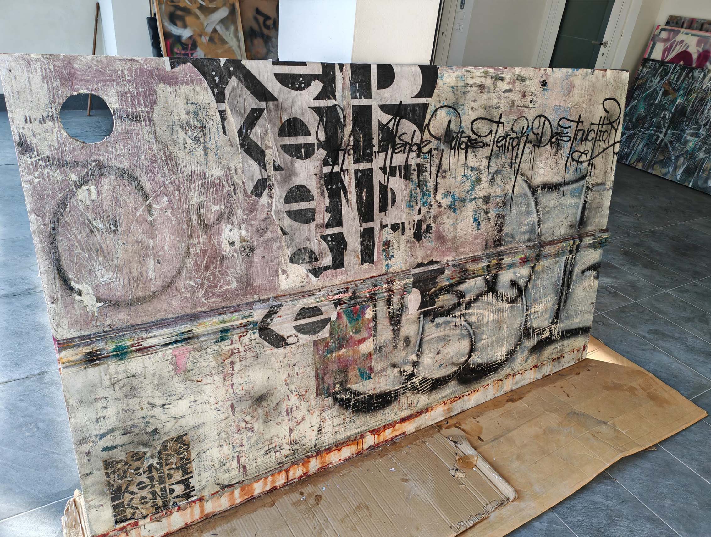 Putas sviluppa il linguaggio della calligrafia urbana attraverso una composizione monumentale e stratificata dove segni, abrasioni e sovrapposizioni costruiscono una superficie pittorica intensa e contemporanea. Il formato panoramico enfatizza la relazione tra scrittura, ritmo e spazio architettonico, mantenendo la tensione visiva tipica della ricerca di Kende.